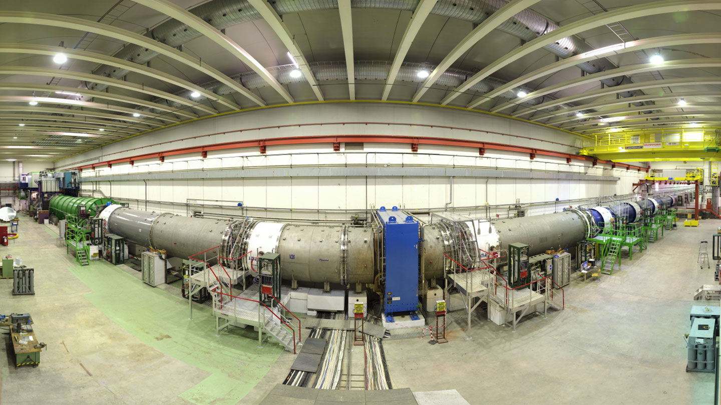 A long cylindrical particle physics experiment is shown in a wide-angle image.